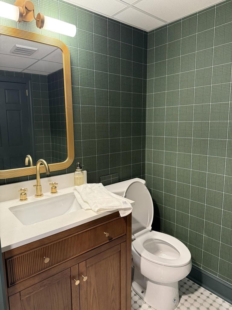 Swanson Interiors bathroom with green grid wallpaper, warm wood cabinetry, and brass fixtures